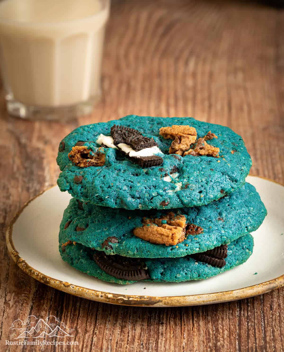 Stack of 3 cookie monster cookies on a plate with milk