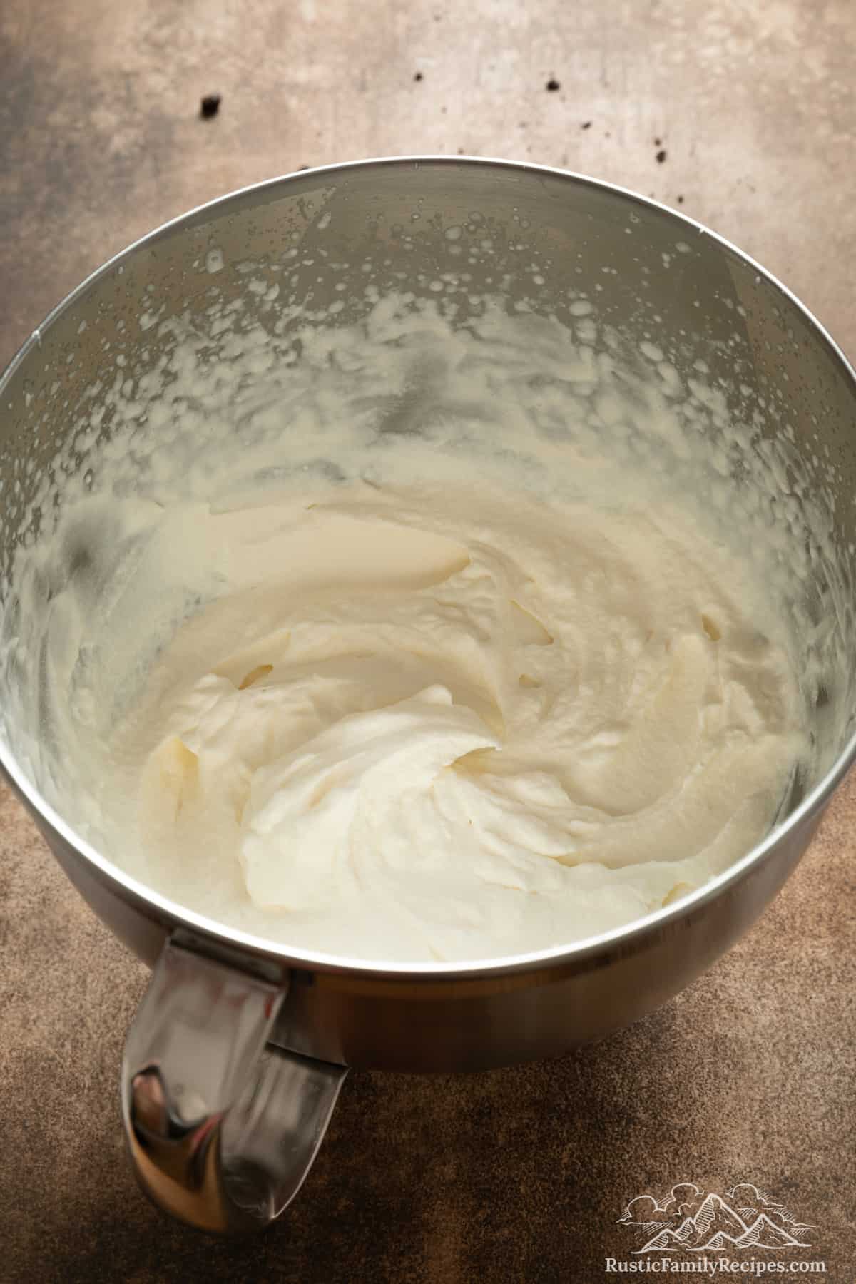 Whipped cream in the bowl of a stand mixer.