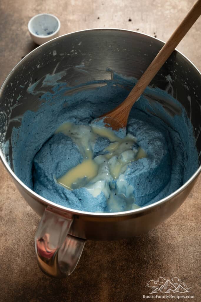 Blue matcha powder is stirred into whipped cream with a wooden spoon for the Cookie Monster ice cream base.