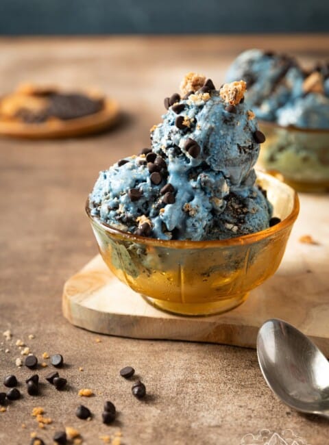 Three scoops of Cookie Monster ice cream in a bowl next to a spoon.