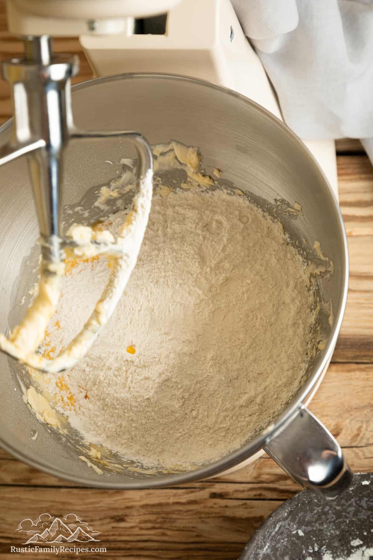 Dry ingredients are added to the wet ingredients for cake batter inside the bowl of a stand mixer.