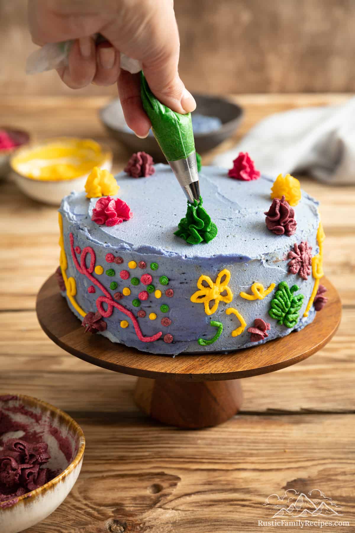A hand pipes frosting swirls on top of a decorated Encanto cake.