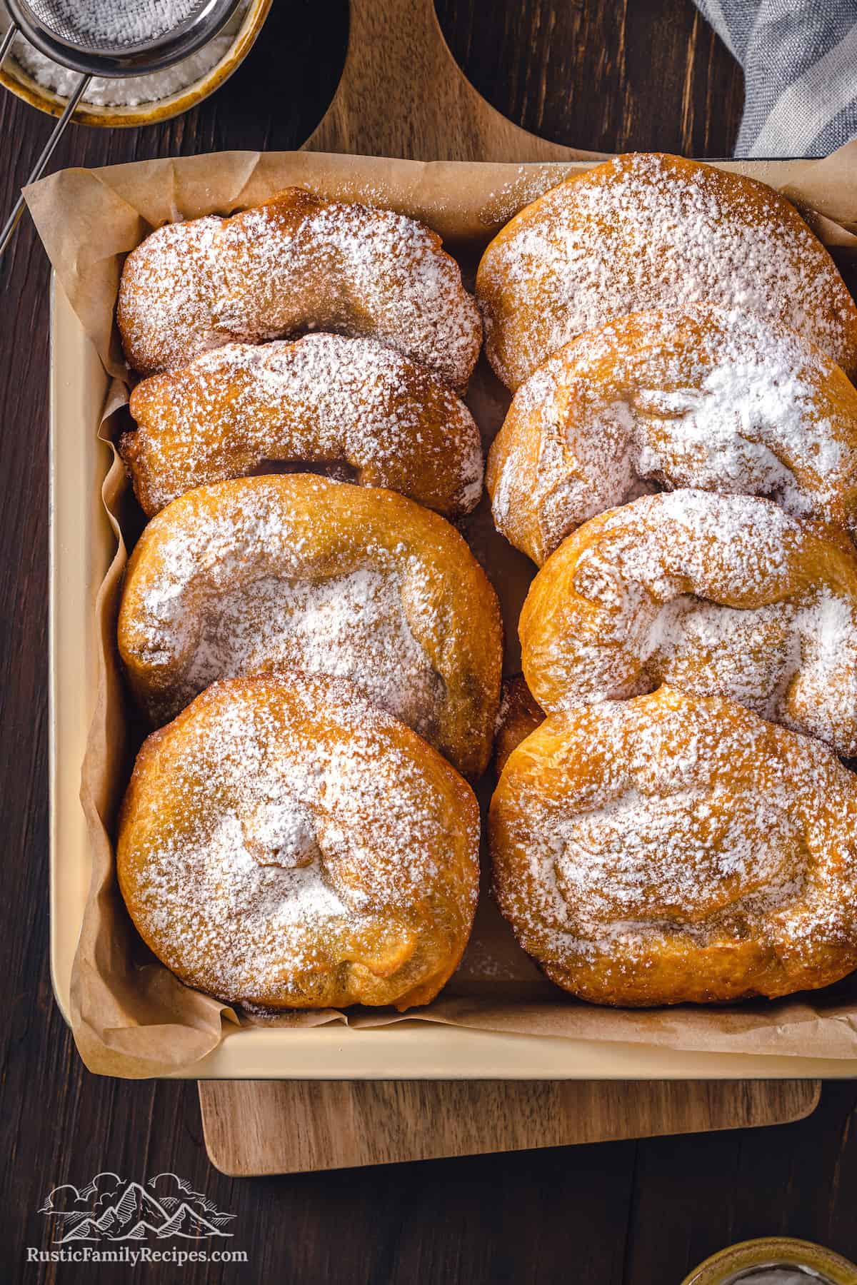 Two rows of hojaldres dusted with powdered sugar, nestled inside a square basket.