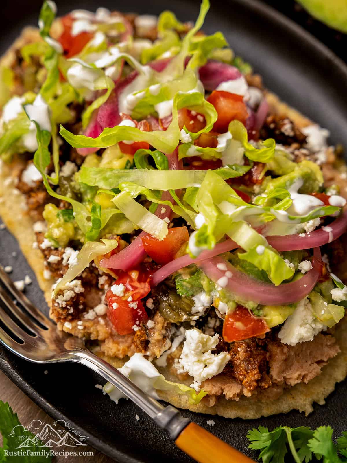 Close up of huaraches assembled with toppings on a black oval plate.