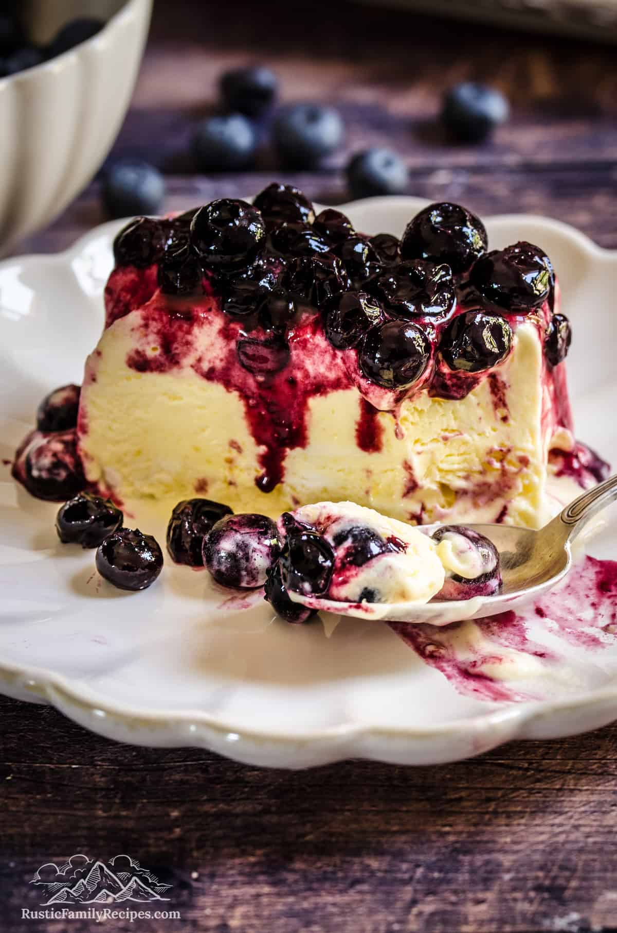 A slice of lemon blueberry semifreddo on a plate, topped with blueberry sauce next to a spoonful of semifreddo..