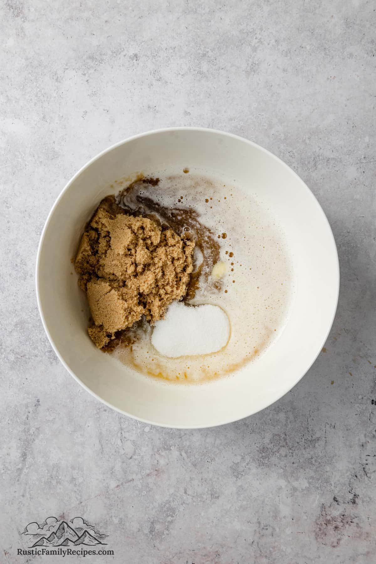 Brown sugar and white sugar combined in a bowl with melted butter.