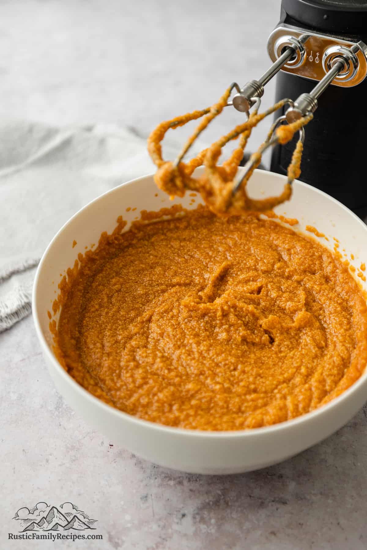 The beaten wet ingredients for pumpkin cookie dough in a bowl next to an electric mixer.