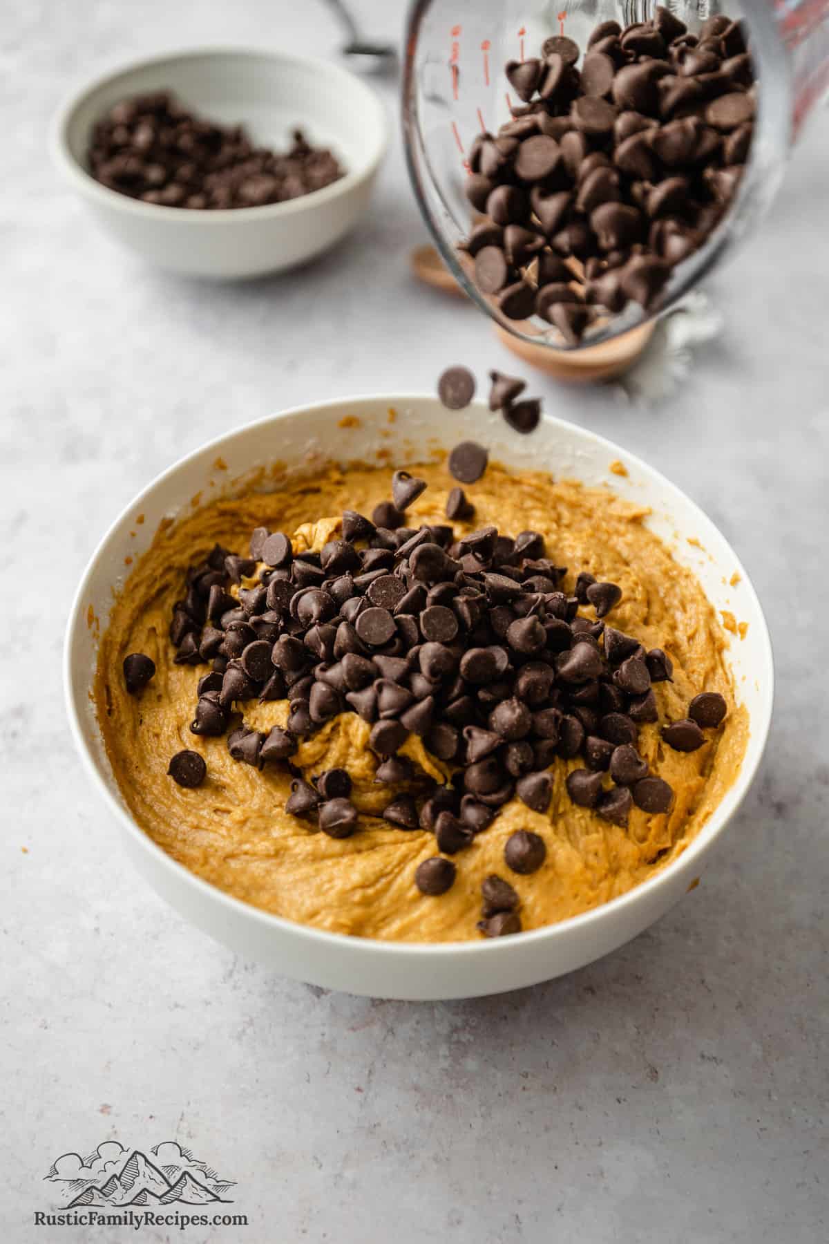 Chocolate chips are added to pumpkin cookie dough in a mixing bowl.