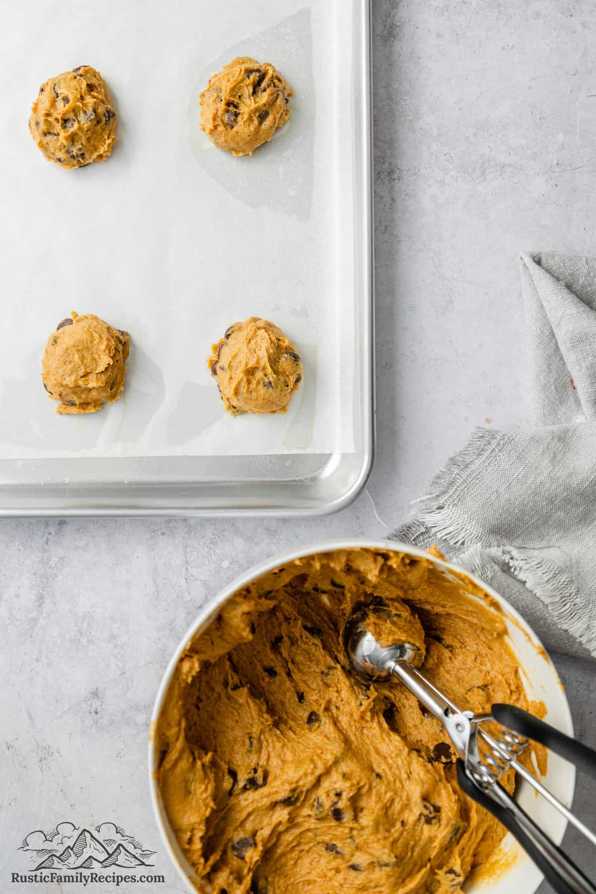 A cookie scoop portions pumpkin chocolate chip cookie dough from a bowl onto a lined baking sheet.