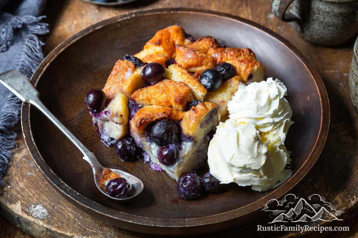A slice of blueberry bread pudding on a plate with ice cream and whipped cream
