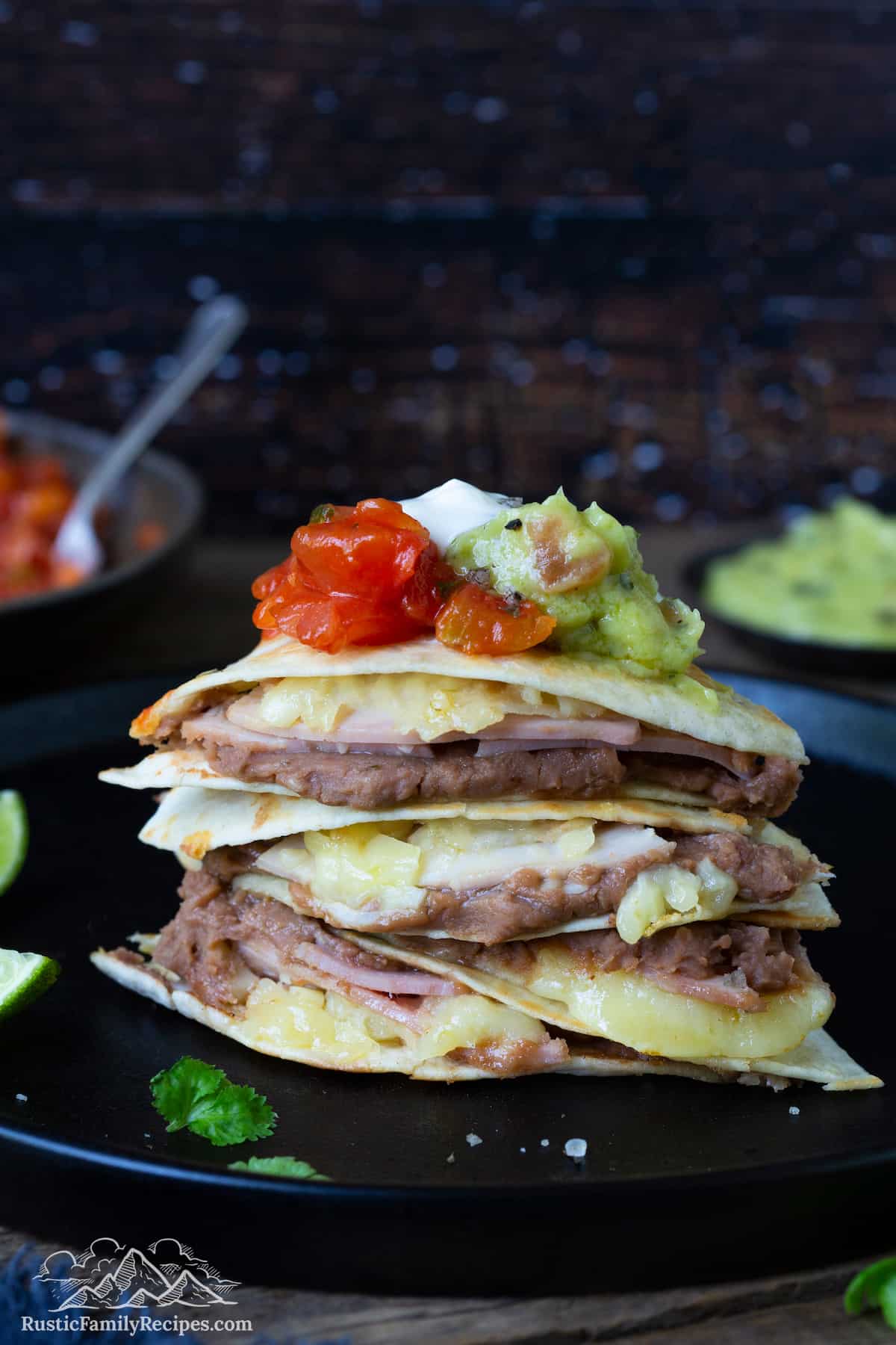 A stack of sincronizadas topped with sour cream, guacamole, and salsa.