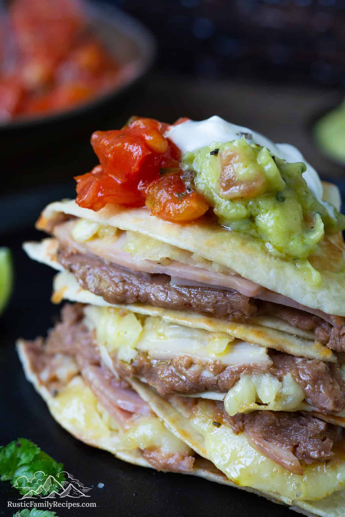 Close up of a stack of sincronizadas topped with sour cream, guacamole, and salsa.