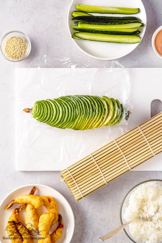 Arranging the avocado on top of the roll, covered with plastic wrap.