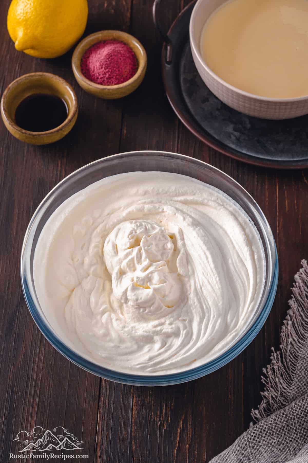 Whipped cream in a large mixing bowl, next to small bowls of food coloring and a bowl of condensed milk.
