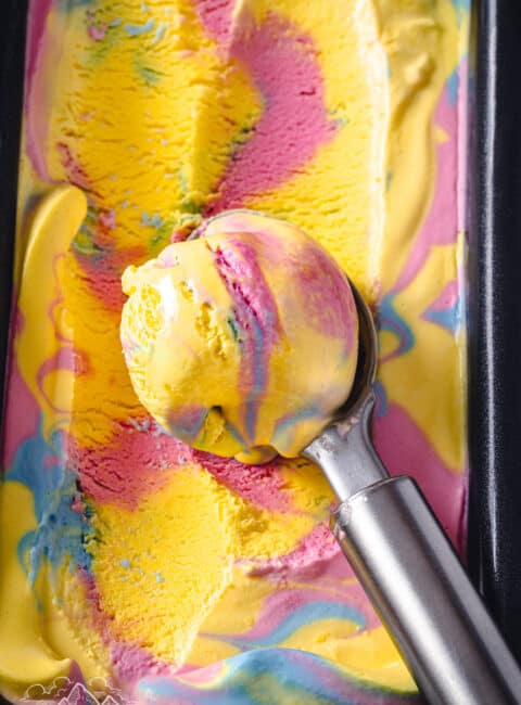 Close up of an ice cream scoop of Superman ice cream resting on a loaf pan filled with ice cream.