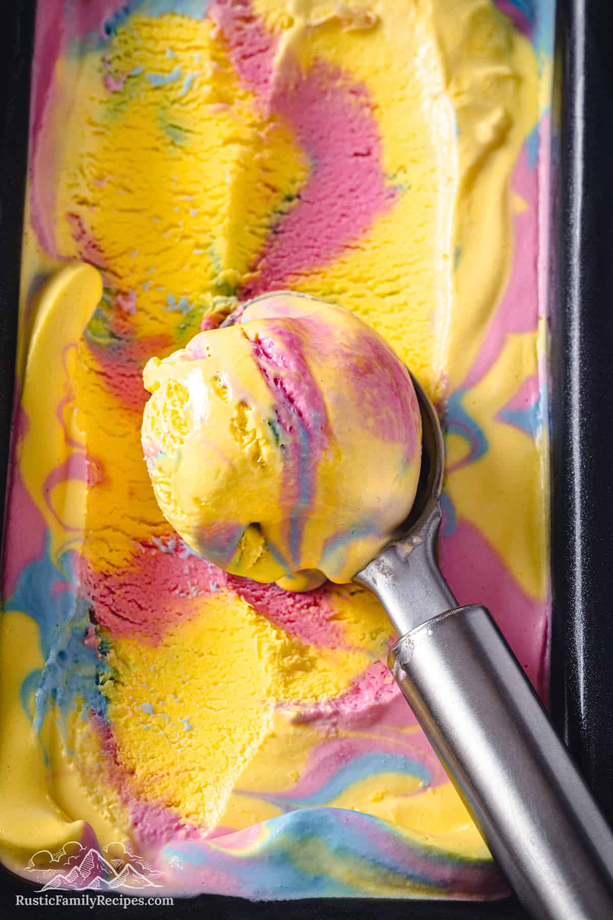 Close up of an ice cream scoop of Superman ice cream resting on a loaf pan filled with ice cream.