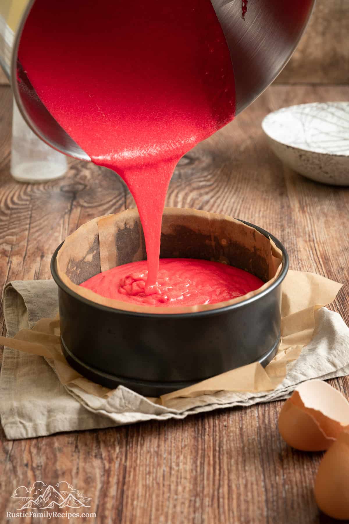 Pink cake mix is poured into a cake pan.