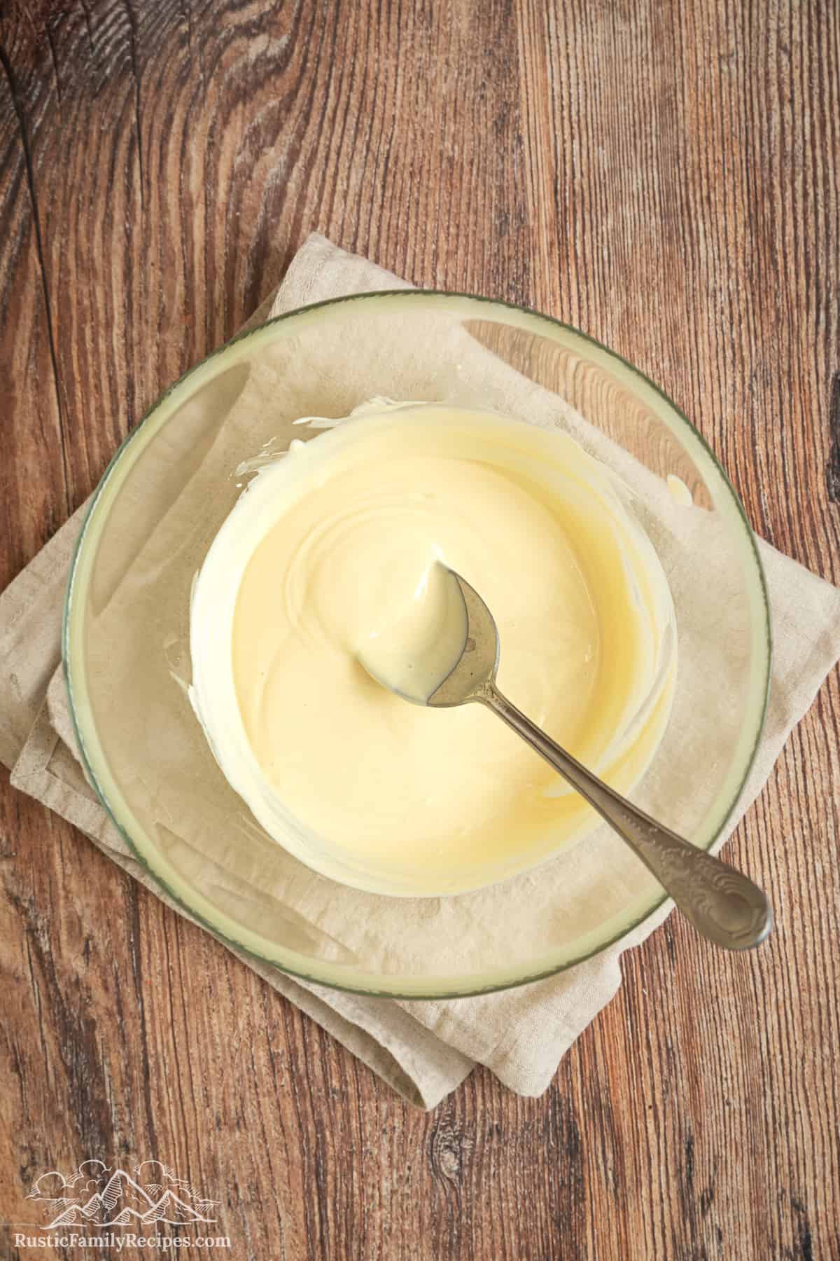 Melted white chocolate in a glass bowl with a spoon.
