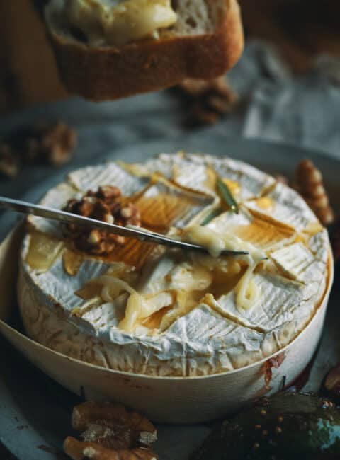 A knife scooping baked camembert cheese with honey and walnuts