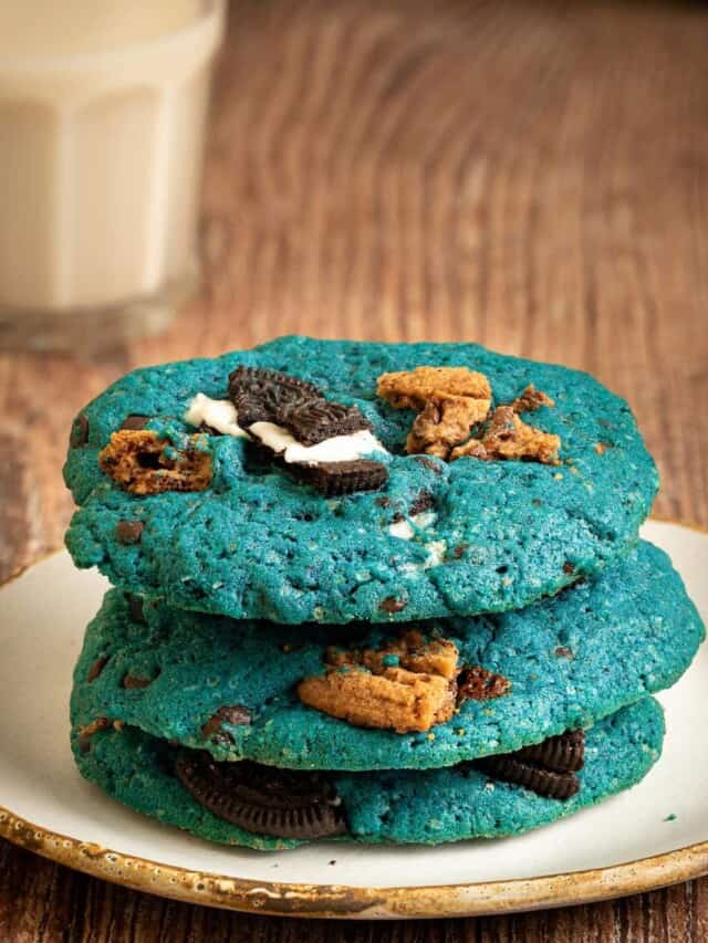 Stack of 3 cookie monster cookies on a plate with milk