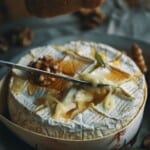 A knife scooping baked camembert cheese with honey and walnuts