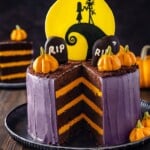 Purple frosted Nightmare Before Christmas cake with a missing slice displayed on a wooden table.