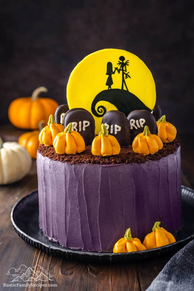 Nightmare Before Christmas cake decorated with purple buttercream, orange buttercream pumpkins, chocolate graveyard cookies, and a Spiral Hill topper.