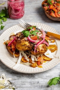 Honduran pollo con tajadas served with fried plantain, pickled onion, shredded cabbage, chismo, pink sauce, and tomato sauce.
