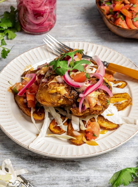 Honduran pollo con tajadas served with fried plantain, pickled onion, shredded cabbage, chismo, pink sauce, and tomato sauce.