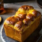 A loaf of pumpkin brioche cooling on a wooden tray