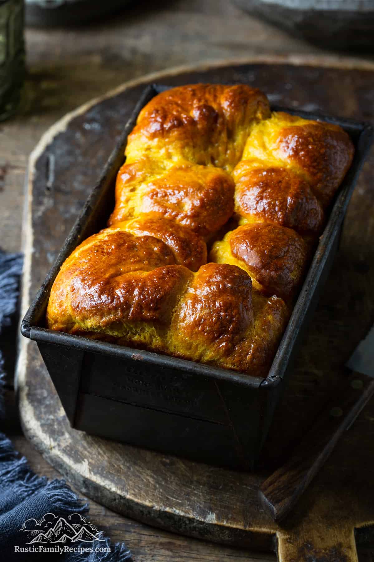 A loaf of pumpkin brioche fresh out of the oven cooling on a wooden tray.
