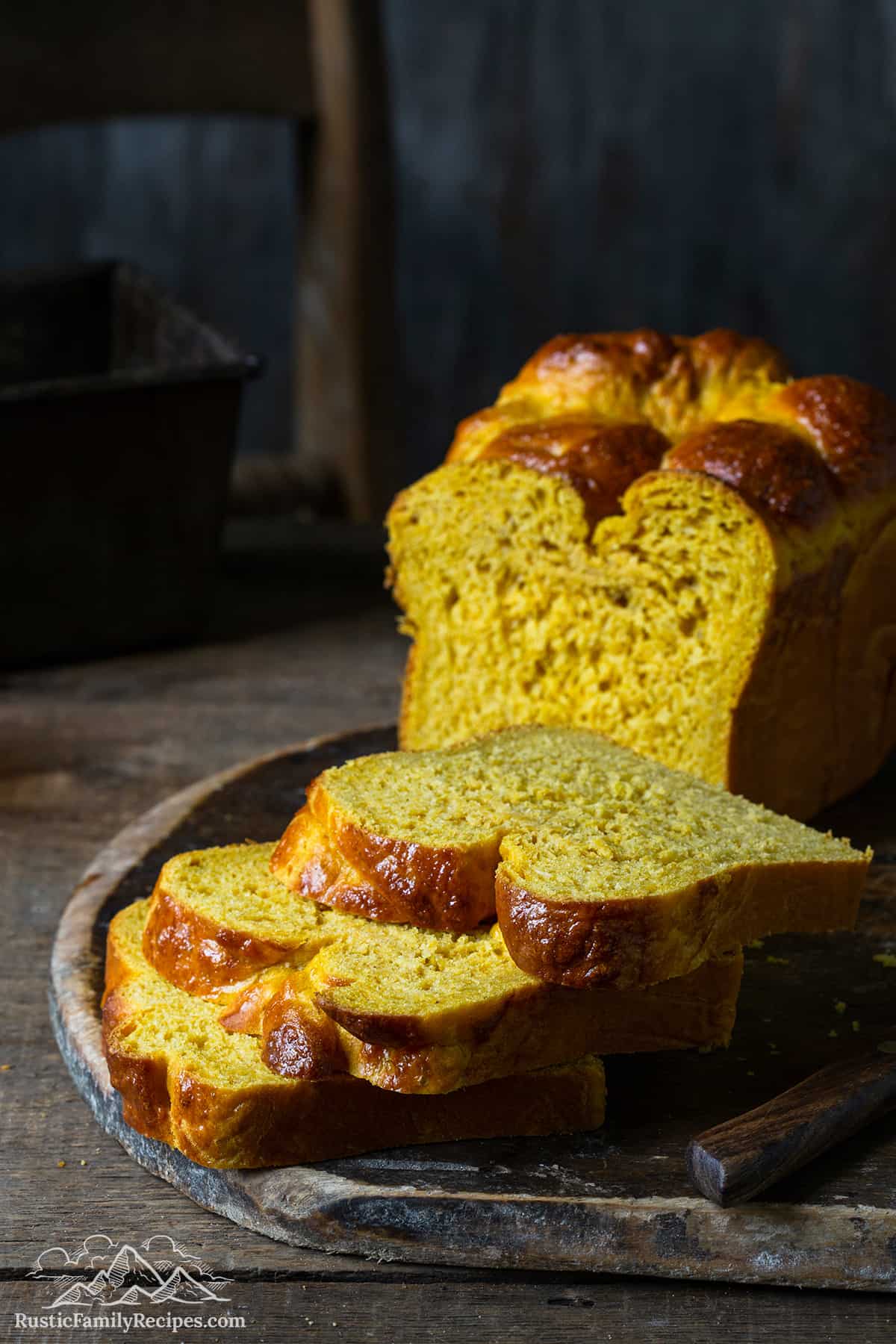 A loaf of pumpkin brioche bread cut into slices on a wood tray.
