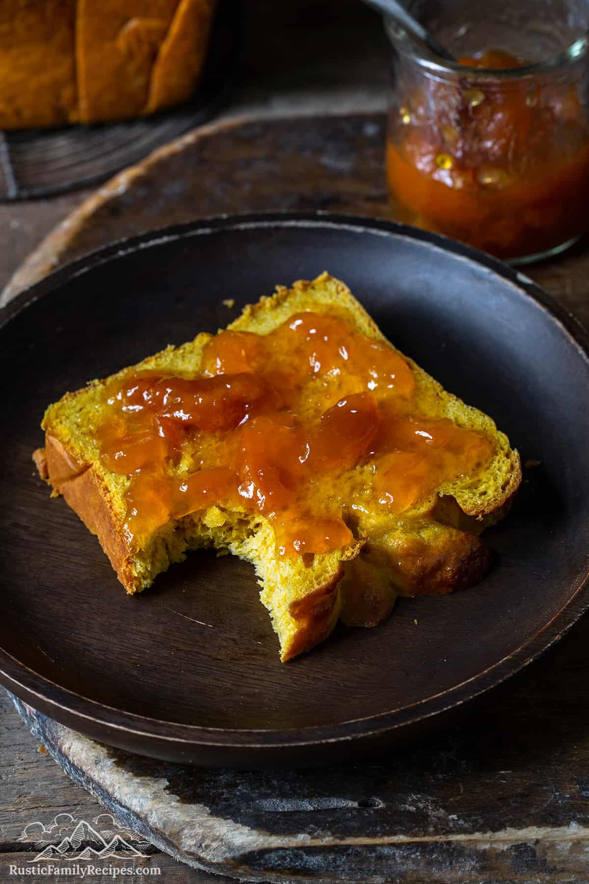 A slice of pumpkin brioche slathered with jam with a big bite missing.