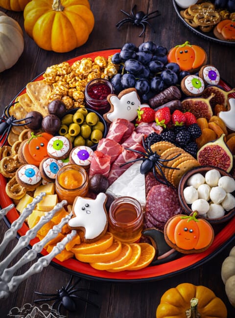 A halloween themed charcuterie board with a skeleton hand and small pumpkins