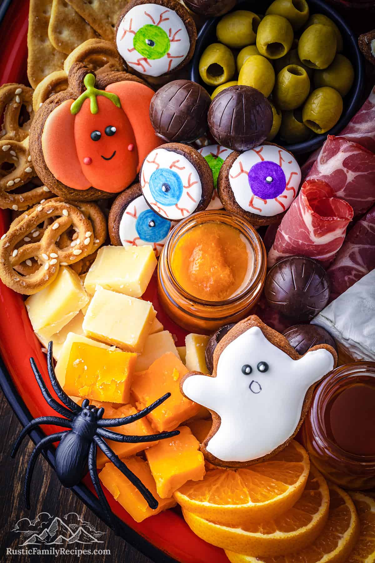 A halloween themed charcuterie board with a plastic spider and ghost cookies.