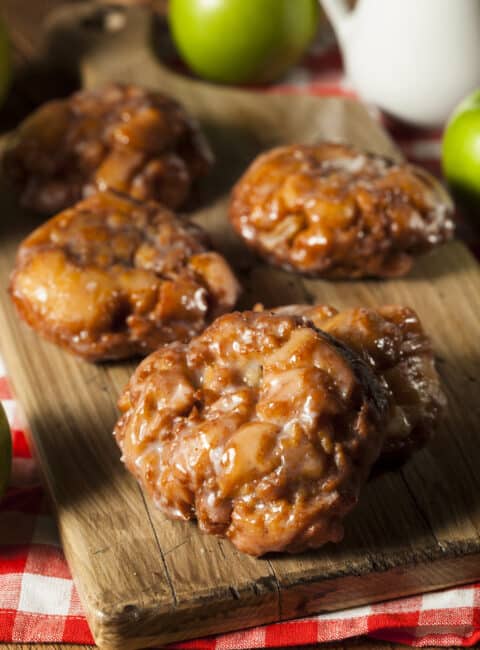 3 apple fritters on a wood cutting board