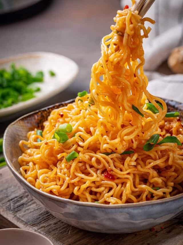 Spicy ramen noodles in a bowl with chopsticks picking up a bite full