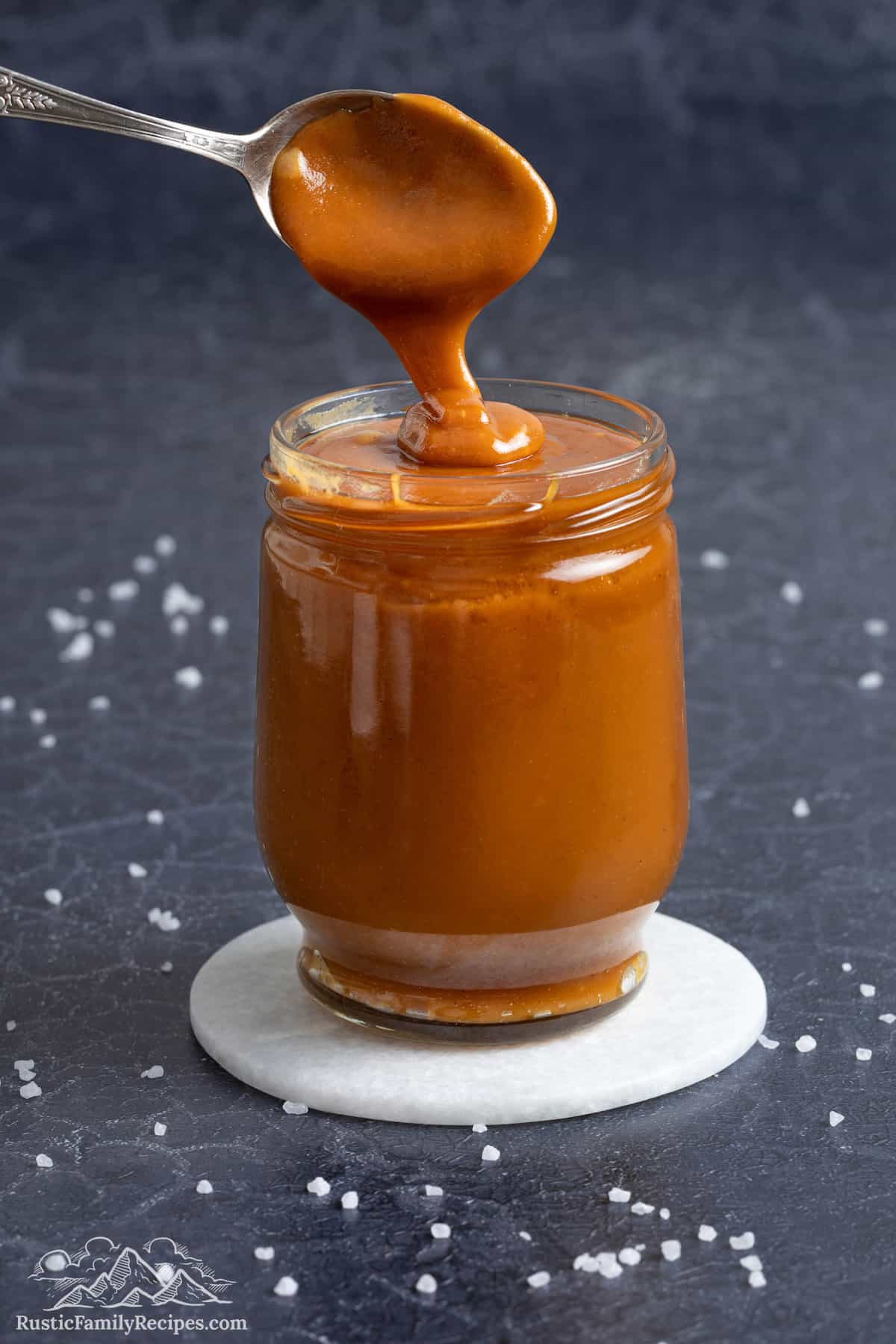 Salted caramel sauce drizzling from a spoon to a glass jar.