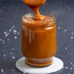 Salted caramel sauce drizzling from a spoon to a glass jar.
