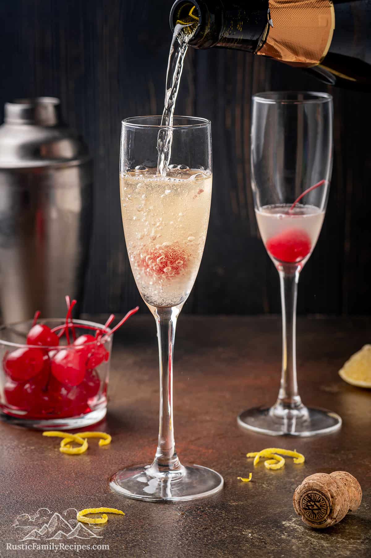 Two champagne glasses with cherries, champagne being poured into one.