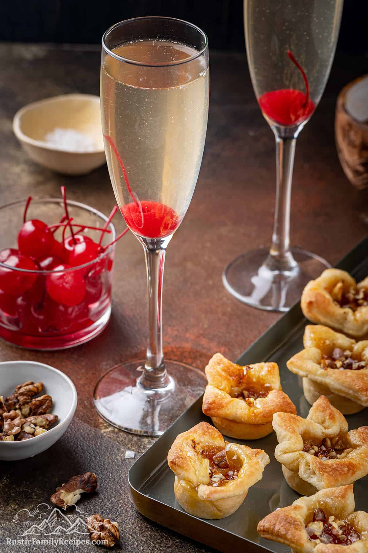 Two french 76 cocktails next to a tray of brie bites