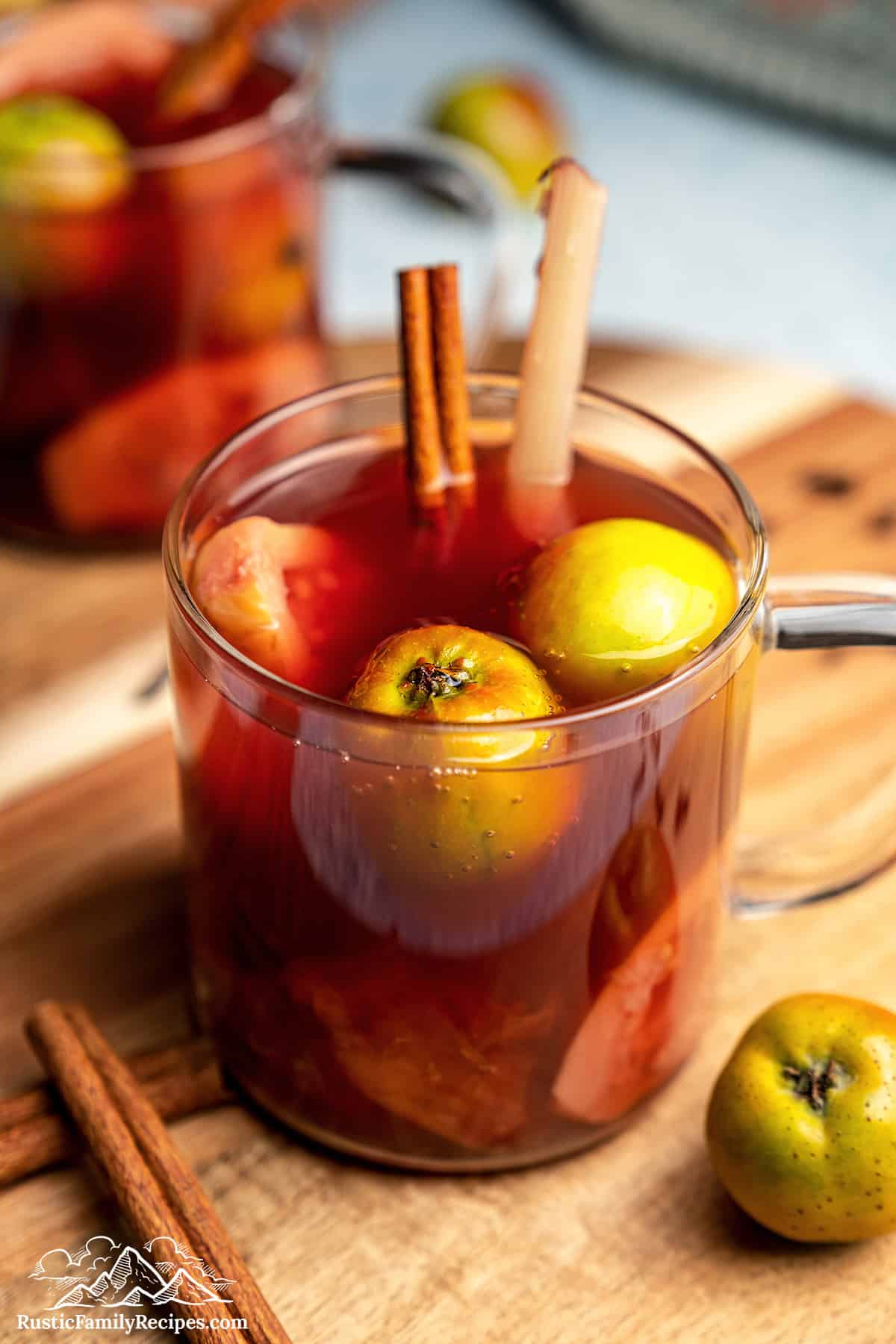 Ponche de frutas navideño in a glass cup with fruit and a cinnamon stick.