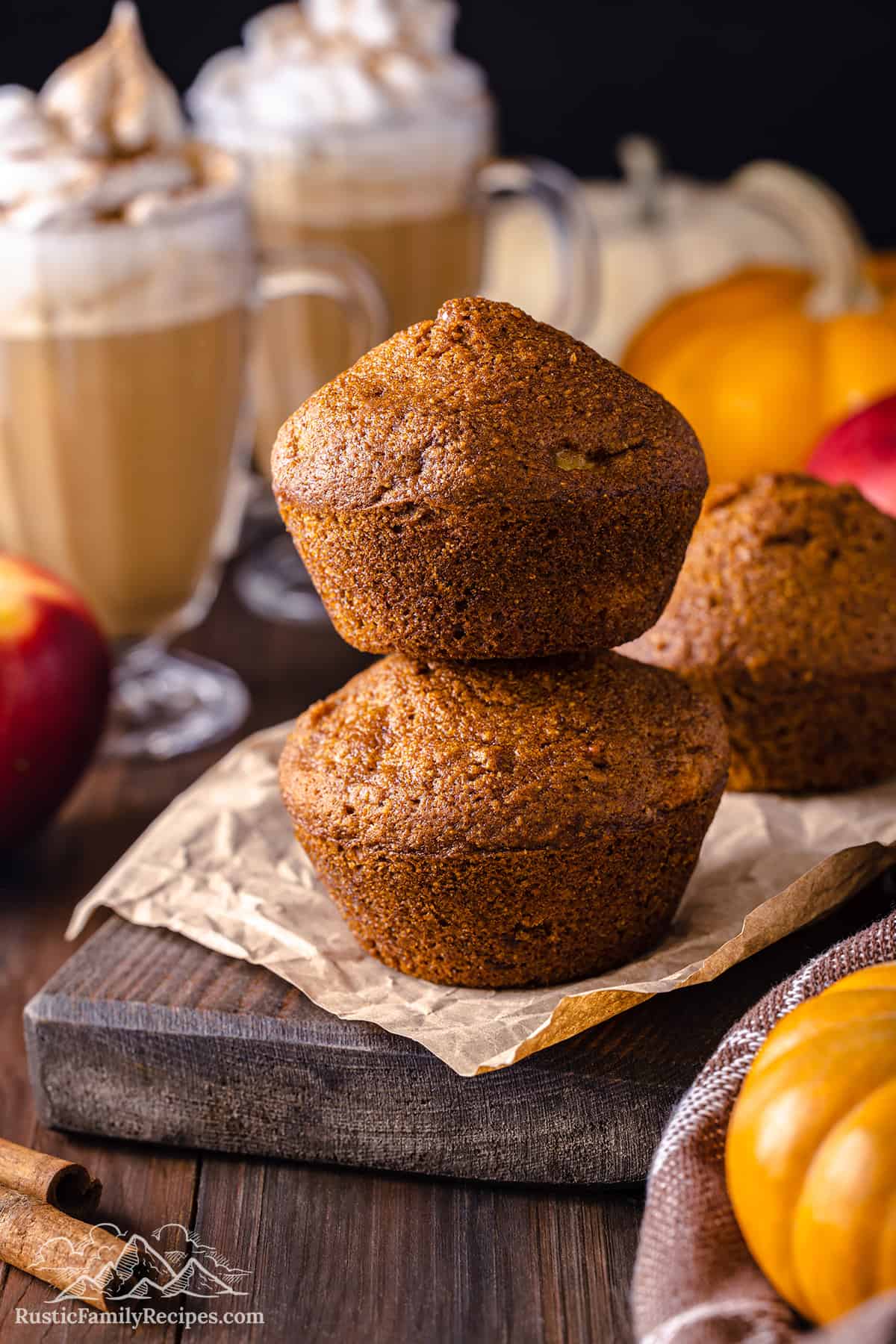 Two Pumpkin Apple Muffins stacked on top of each other next to pumpkin spice lattes