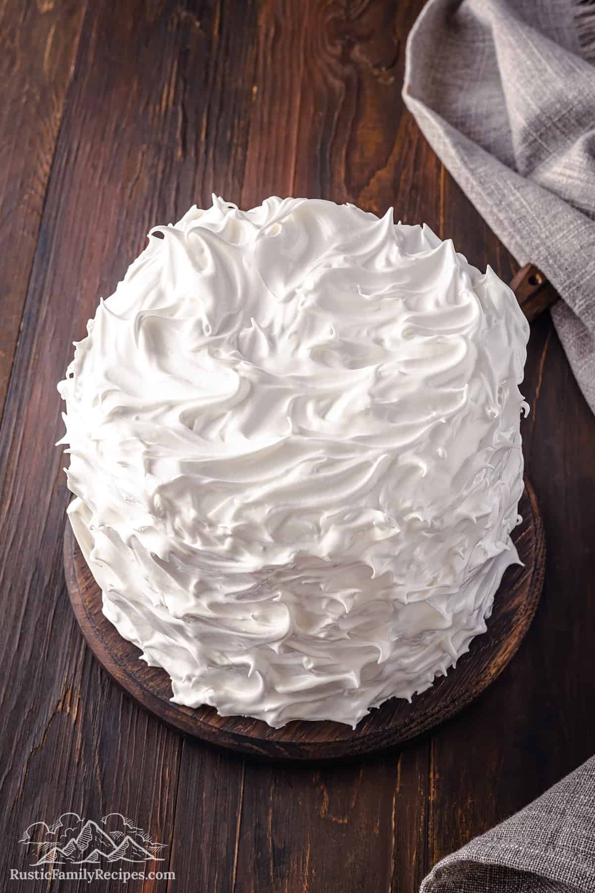 Assembled cake coated with marshmallow frosting swirls.