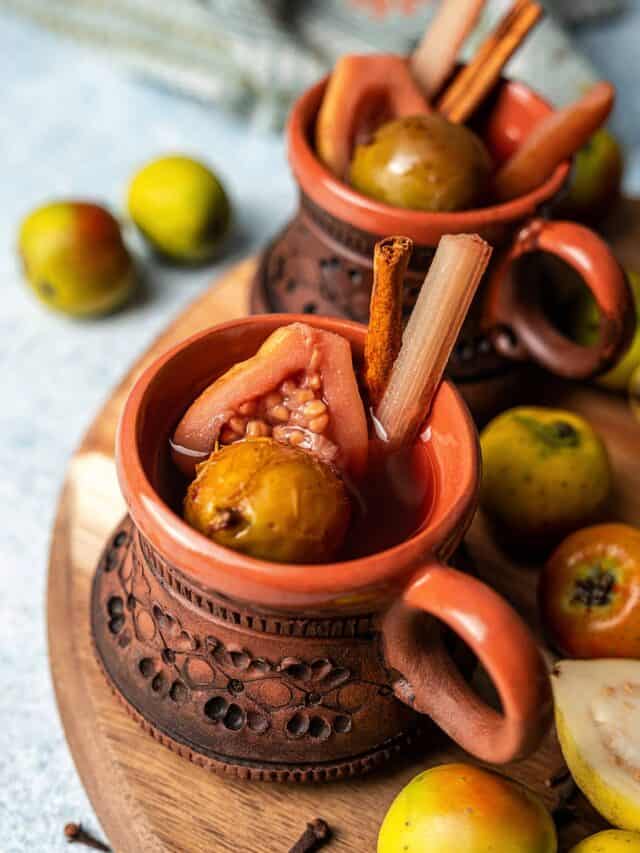 Ponche de frutas navideño in a cup, served with fruit and a cinnamon stick.