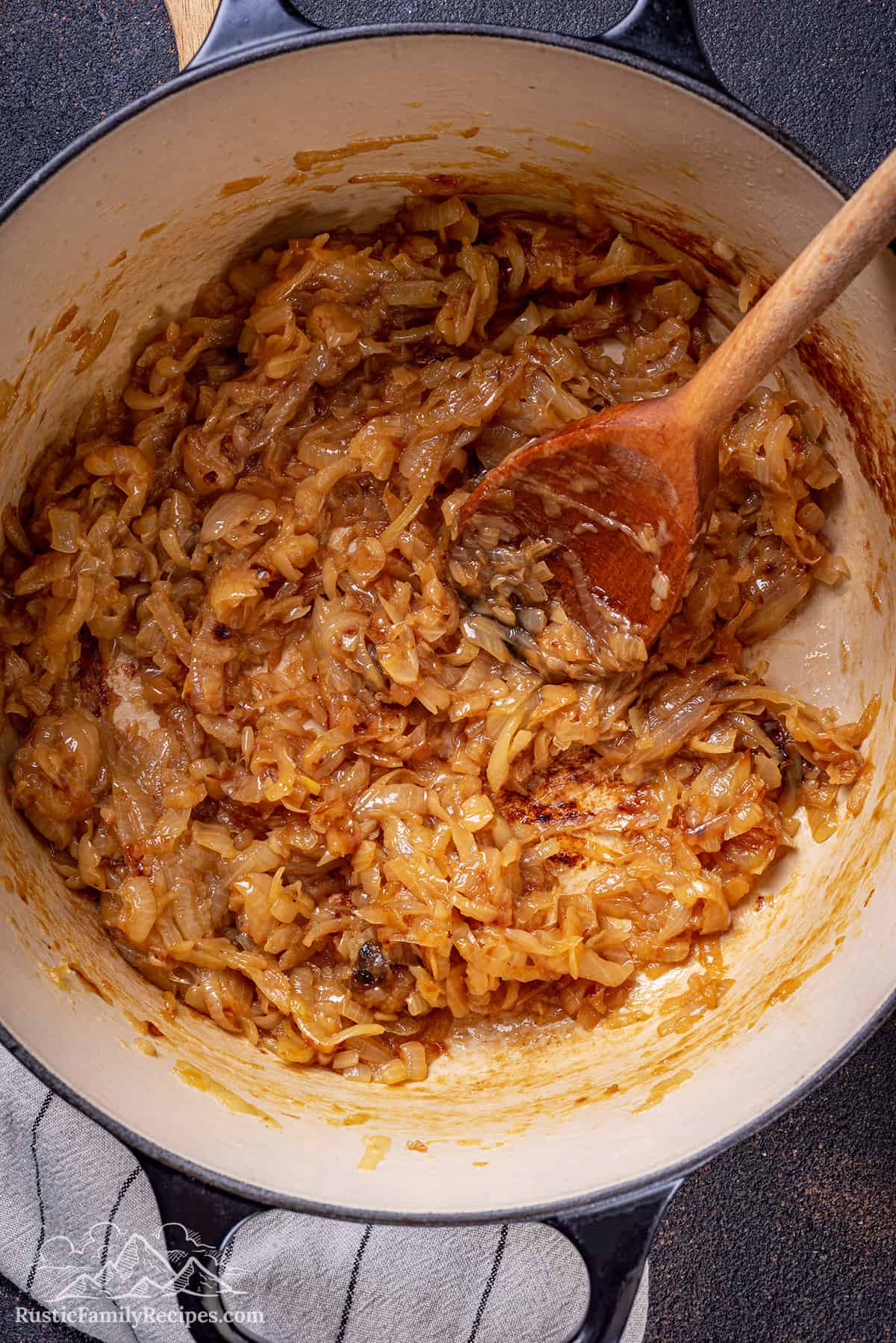 Caramelized onions in a dutch oven with a wooden spoon