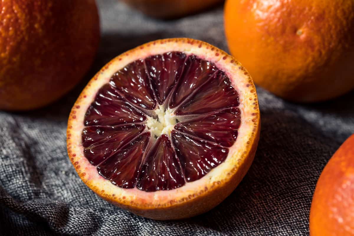 Blood oranges on a grey background, one sliced in half to show the insides