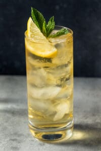 A green tea highball cocktail in a glass with ice, lemon wedge and mint