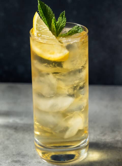 A green tea highball cocktail in a glass with ice, lemon wedge and mint