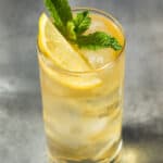 A green tea highball cocktail in a glass with ice, lemon wedge and mint